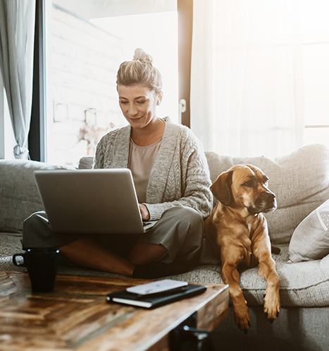 Businesswoman working on laptop computer sitting at home with a dog.