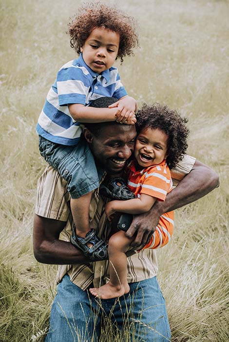 Two smiling children hug their father as they have fun playing outside.