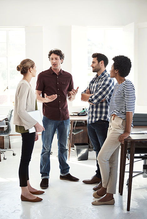 Group of coworkers stand in conference room engaged in a conversation.