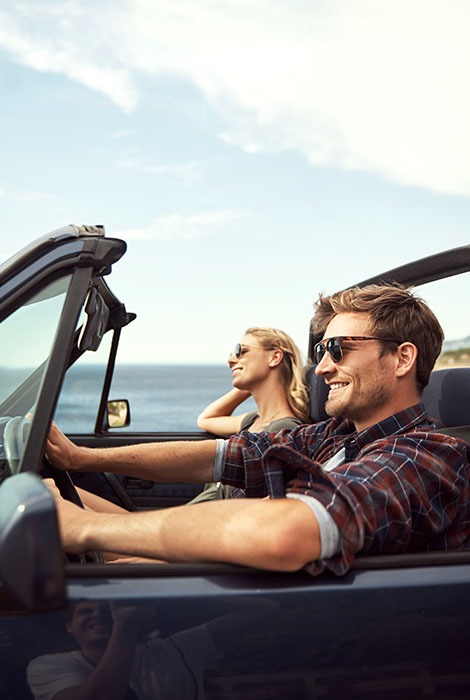 Smiling expat couple drives down coast with the top down in their convertible.