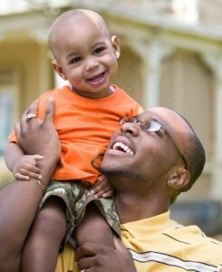 Expat man smiles with his son on his shoulders.