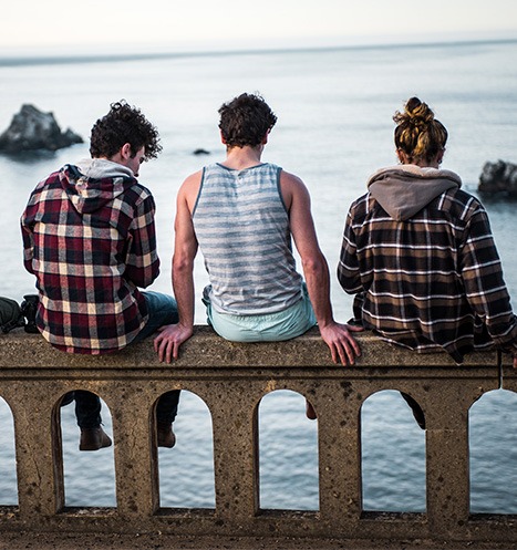 Four young expats admire the sea as they sit atop a stone bridge.