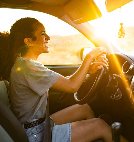 Woman smiles as she is driving her car during a beautiful sunset.