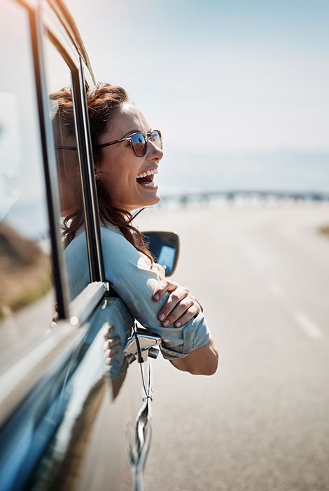 Happy traveler leans out the vehicle window while driving along the coast.