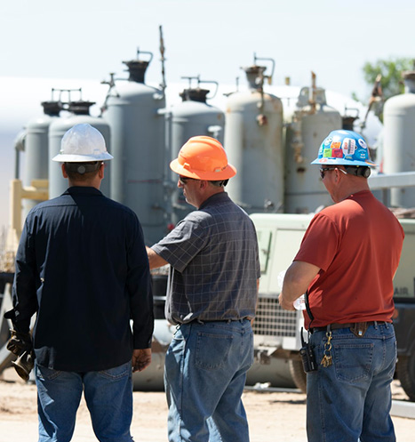 International government contractors in hardhats discuss work plans outside of factory.