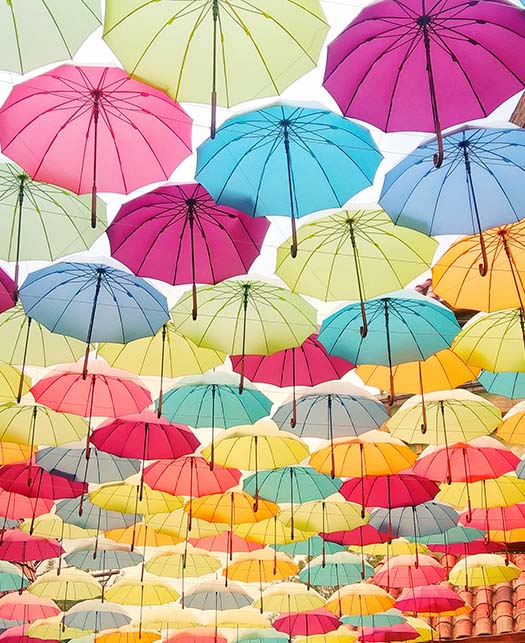 Colorful umbrellas suspended create a canopy of protection for people underneath.