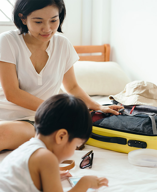 Son plays on phone as mother packs a suitcase for a family trip.