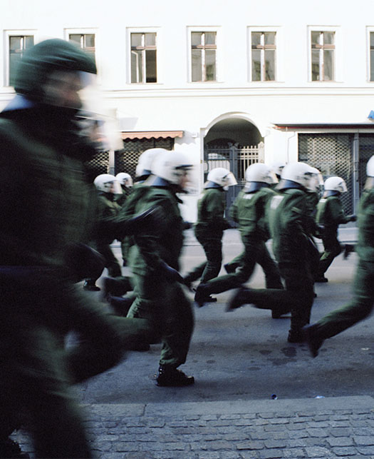 Armed military and police force running down the street.