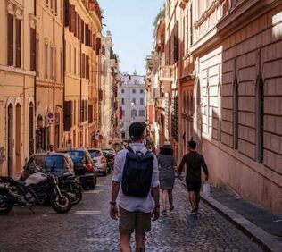 Backpacker takes a stroll down a scenic Italian brick road lined with vehicles.