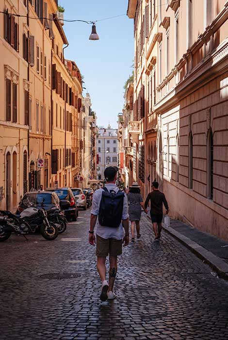 Backpacker takes a stroll down a scenic Italian brick road lined with vehicles.