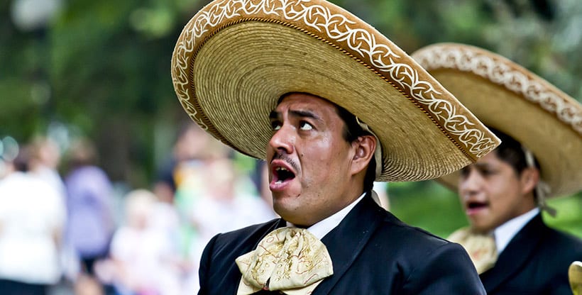 A Mariachi singer clad in traditional clothing, including a bow tie and sombrero, belts out a song.
