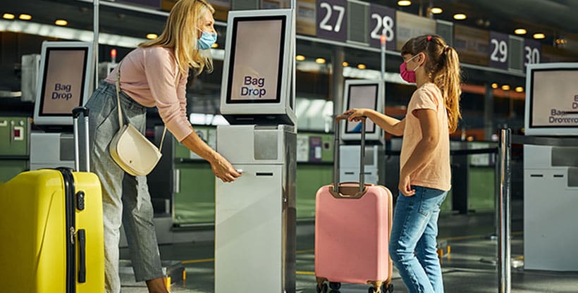 Mother and child check in for their flight at an airport kiosk with their suitcases.