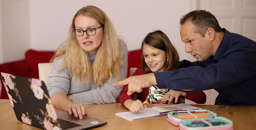 Parents help their child learn a language using a drawing pad and drawing utensils including pencils.