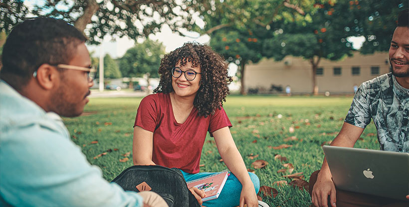 A conversation group of three students sits outdoors learning a new language.