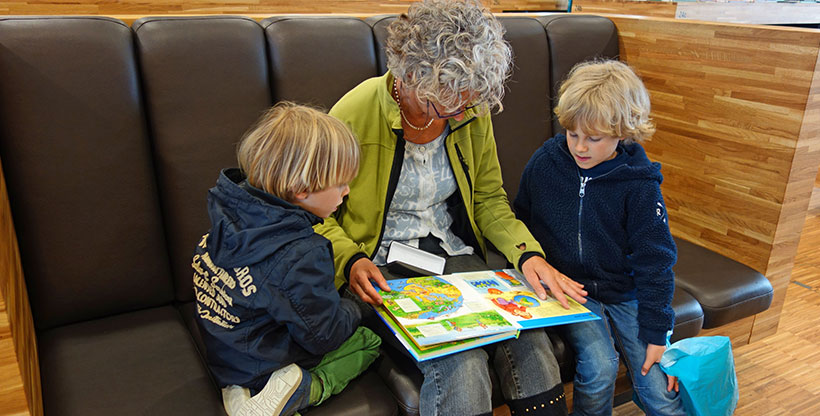 A woman reads a children's book to two young readers, which is a great way for beginners to learn a new language.