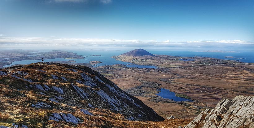 A hiker stands atop a hill with a panoramic view of Ireland’s Connemara National Park's coastline.