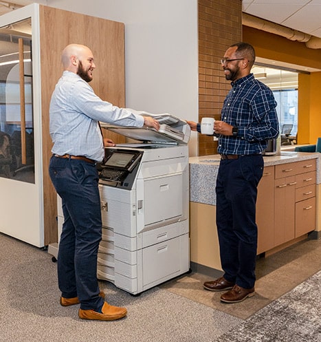 Two insurance agents discuss projects by the printer.