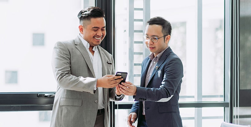 Two insurance professionals chat in a common area at work while looking at a mobile device.