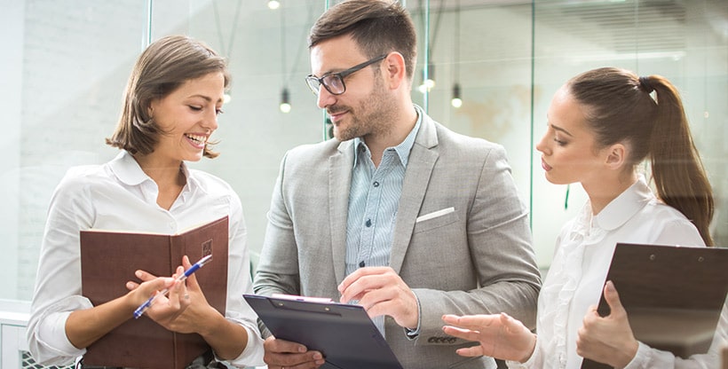 An insurance professional speaks with two colleagues who are viewing documents alongside him.