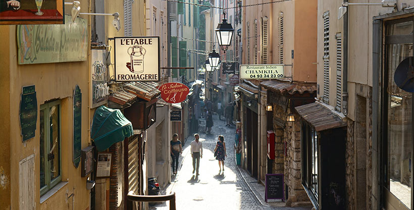People walk in an alleyway lined with shops in France, a country that offers diverse experiences that can be enjoyed by car and on foot.