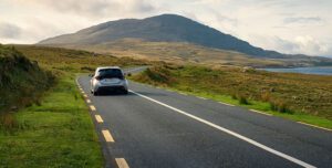 Car driving on an Irish country road with continuous white and broken yellow lines.